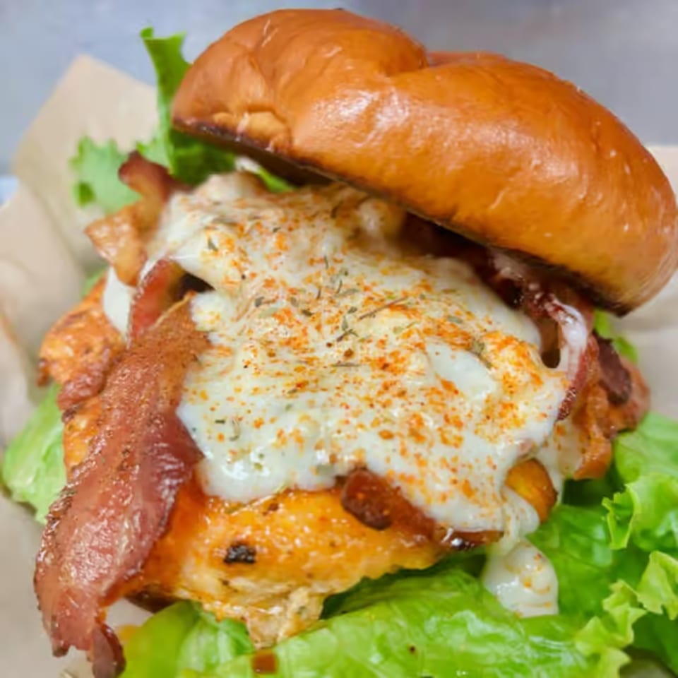 A chicken sandwich with bacon, melted cheese, and lettuce on a brioche bun.